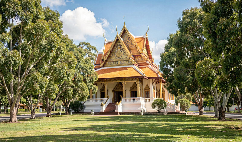 A golden roof of a Thai temple building behind gum trees and green lawns under a bright Queensland sky.